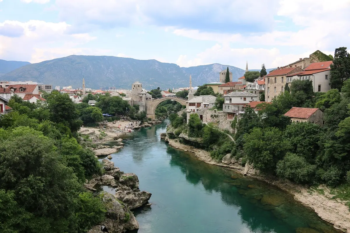 Stari most u Mostaru: Putopis kroz historiju i halal iskustva Koračam kaldrmom starog mostarskog bazara dok se predvečerje lagano spušta nad gradom. Zrakom se širi miris svježe pečenih ćevapa i turske kahve, a negdje u daljini ezan sa minareta najavljuje akšam. Ubrzo se preda mnom ukazuje Stari most – elegantni kameni luk koji stoljećima prkosi vremenu. Njegov odraz treperi na površini rijeke Neretve, stvarajući prizor od kojeg zastaje dah. Dok prilazim, osjećam kako svaki kamen pod mojim nogama priča priču o slavnoj prošlosti i izdržljivosti Mostara – grada nazvanog upravo po čuvarima mostova, mostarima, koji su nekada davno pazili na prelaz preko rijeke.